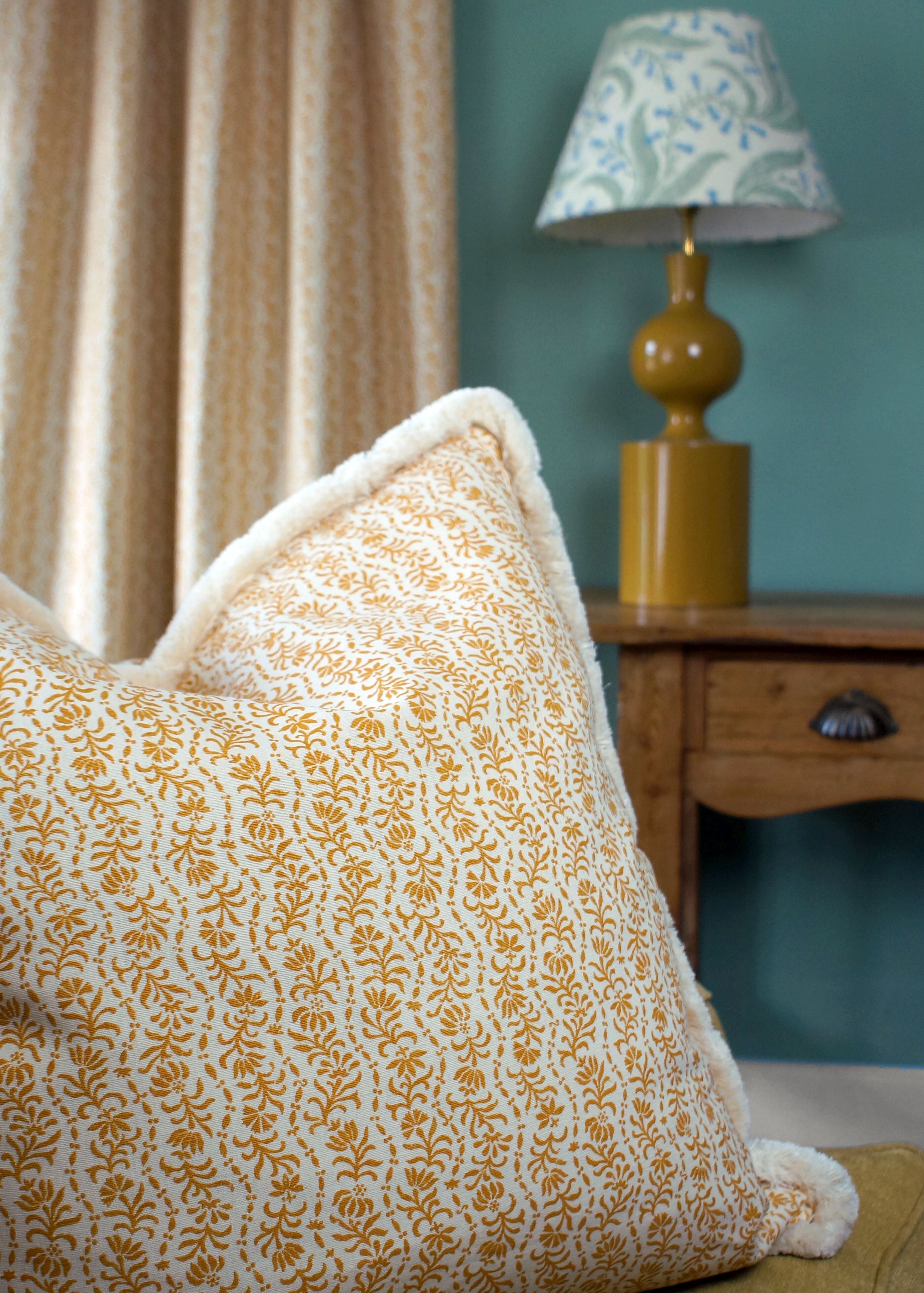 Decorative pillow with floral pattern on a couch, next to a lamp and curtain.