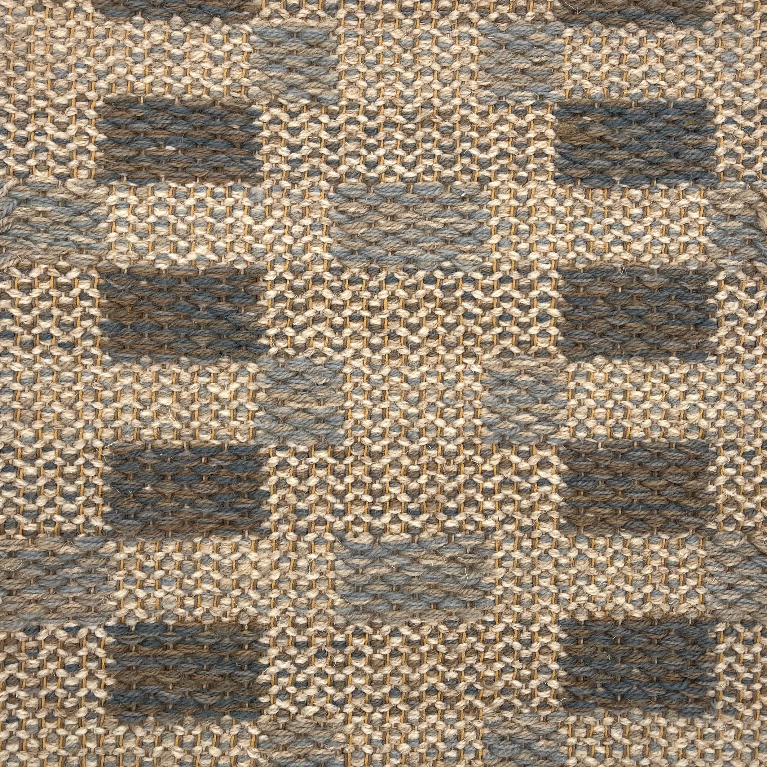 Handwoven rug detail in a checkered design in tan, grey and slate