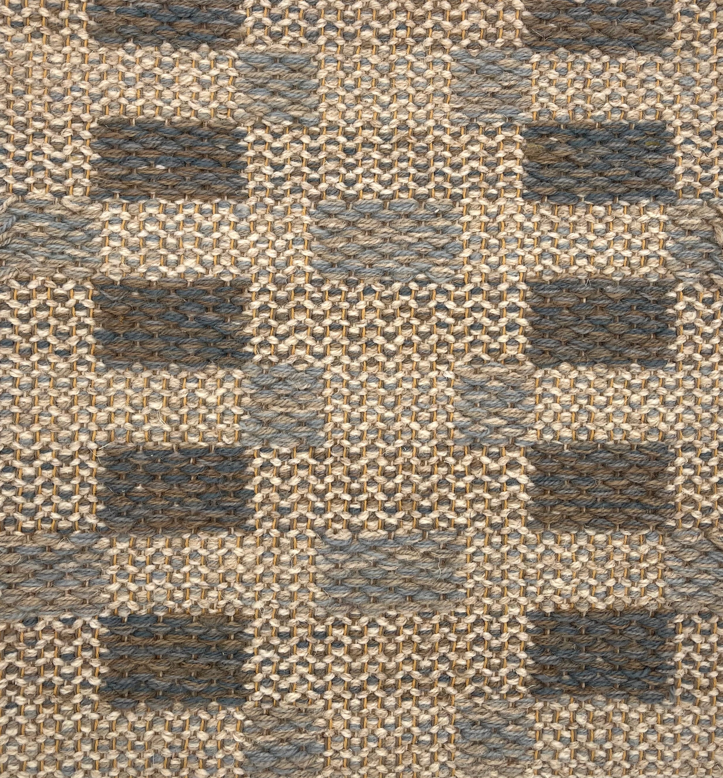 Handwoven rug detail in a checkered design in tan, grey and slate