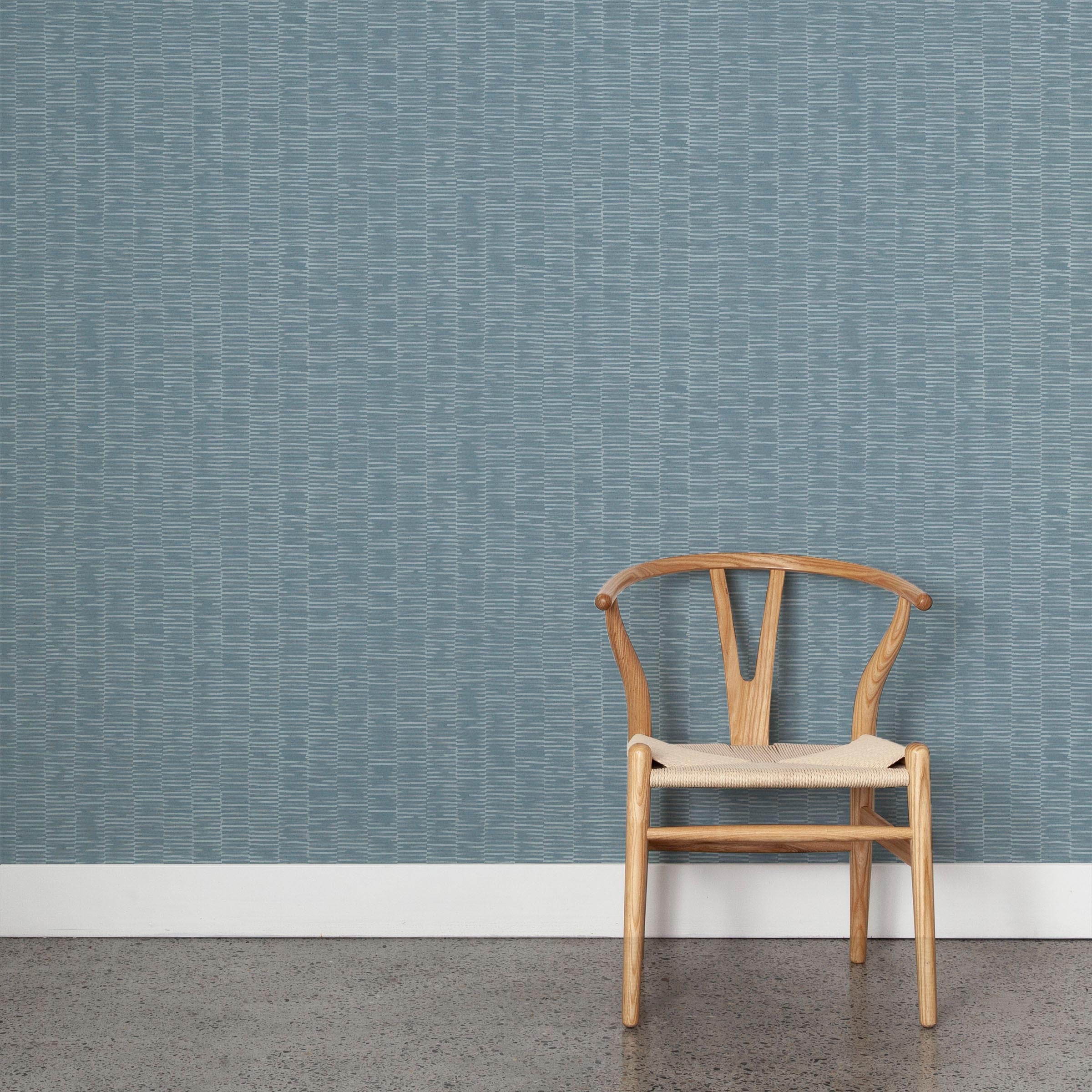 A wooden chair stands in front of a wall papered in a small-scale checked pattern in shades of blue.