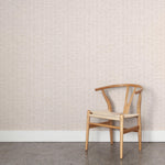 A wooden chair stands in front of a wall papered in a small-scale checked pattern in shades of cream.