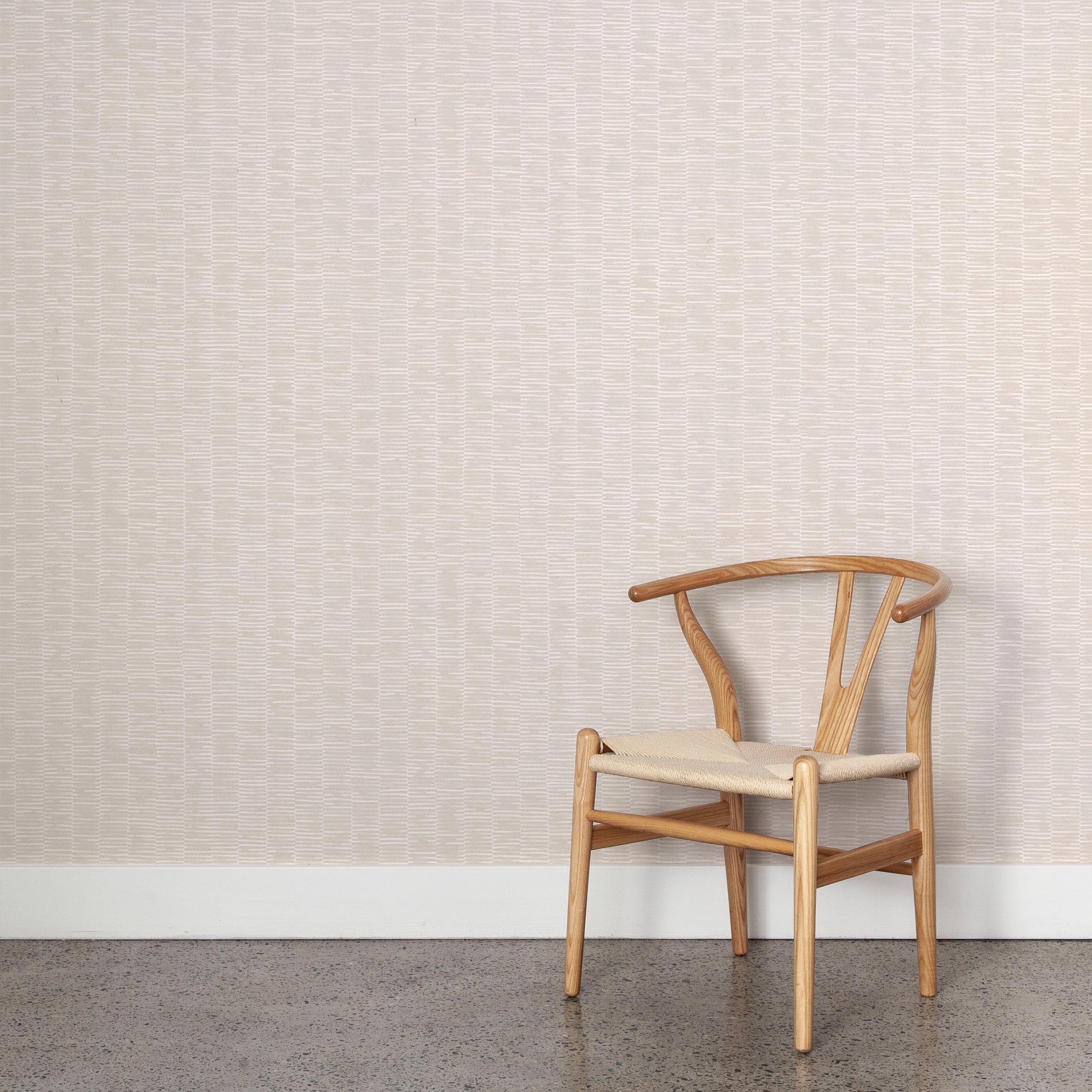 A wooden chair stands in front of a wall papered in a small-scale checked pattern in shades of cream.