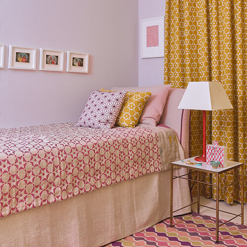 Bedroom with patterned bedspread, yellow curtains, and a side table.