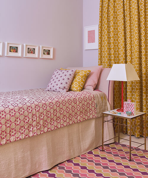Bedroom with patterned bedspread, yellow curtains, and a side table.