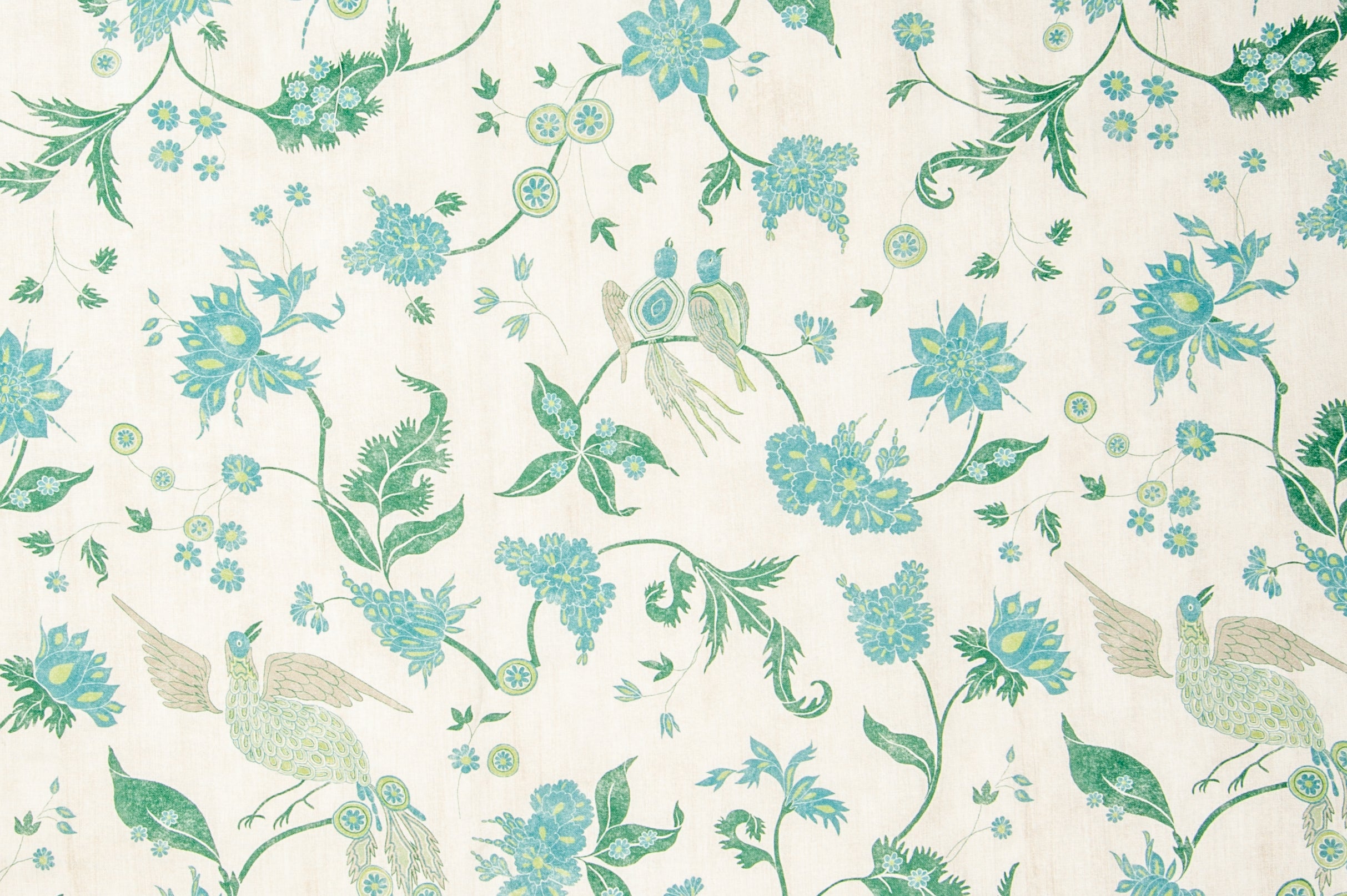 Detail of fabric in a bird and botanical print in shades of green, turquoise and yellow on a cream field.