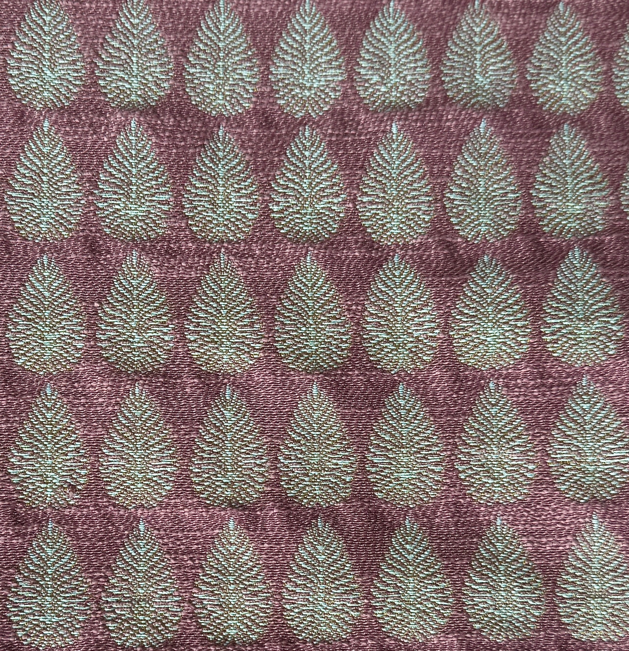 Detail of fabric woven in a repeating leaf print in shades of purple and turquoise.