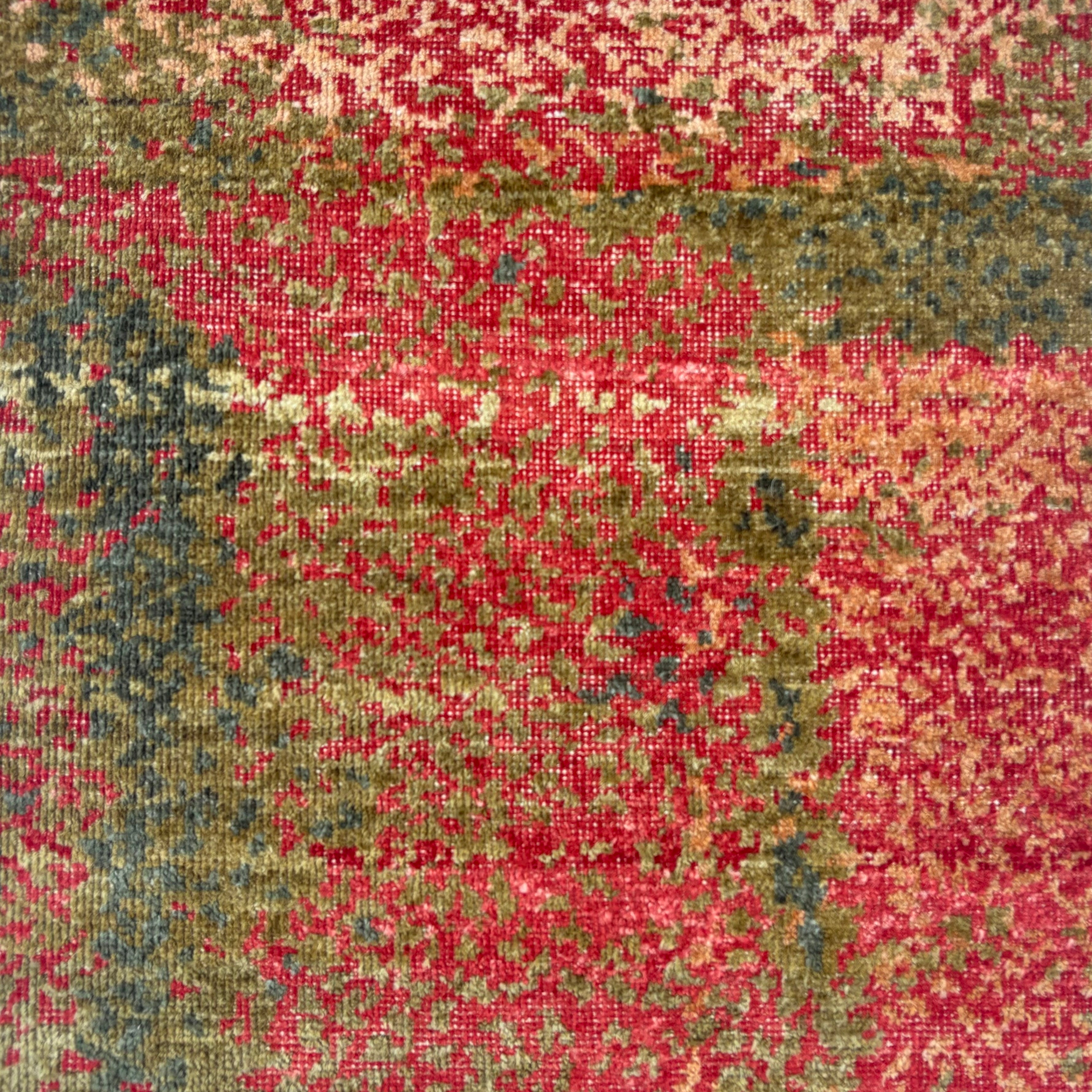 Handknotted rug sample in a pointillist textural design in shades of green, teal and tan on a red field. 