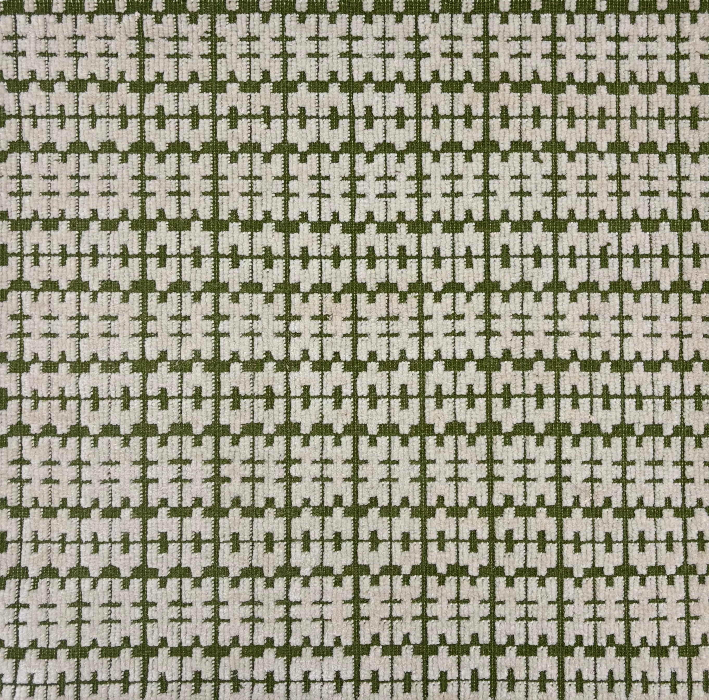 Handowoven rug sampe in a raised geometric pattern in white on a green field. 