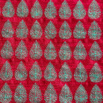 Detail of fabric woven in a repeating leaf print in shades of red and turquoise.