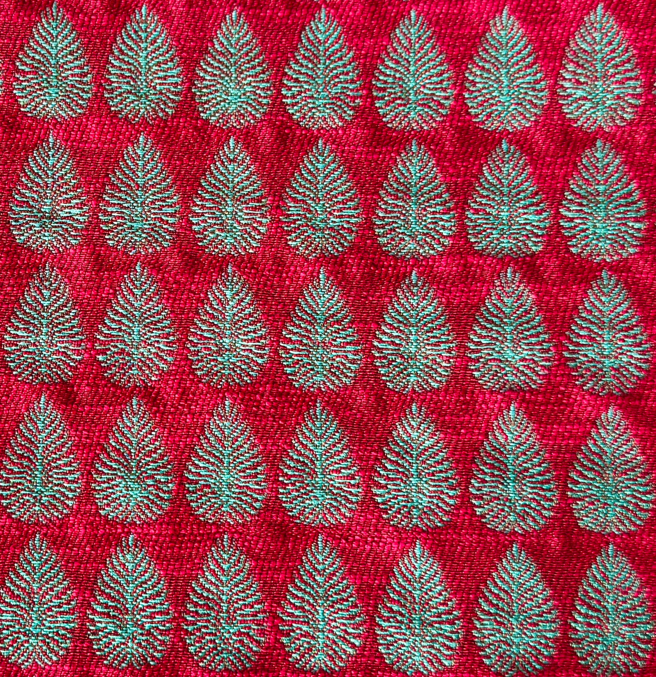 Detail of fabric woven in a repeating leaf print in shades of red and turquoise.