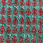 Detail of fabric woven in a repeating leaf print in shades of red and turquoise.