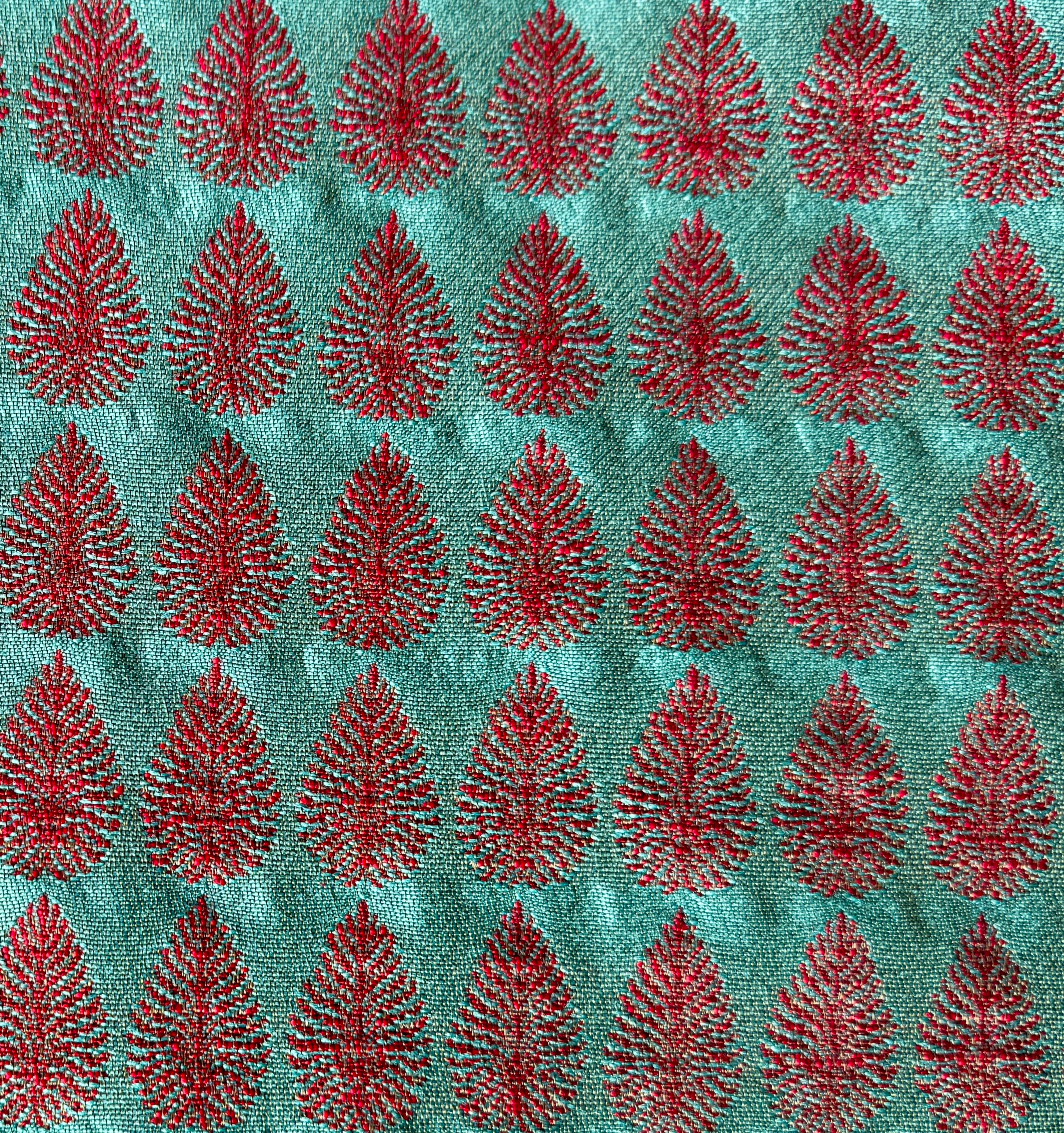 Detail of fabric woven in a repeating leaf print in shades of red and turquoise.