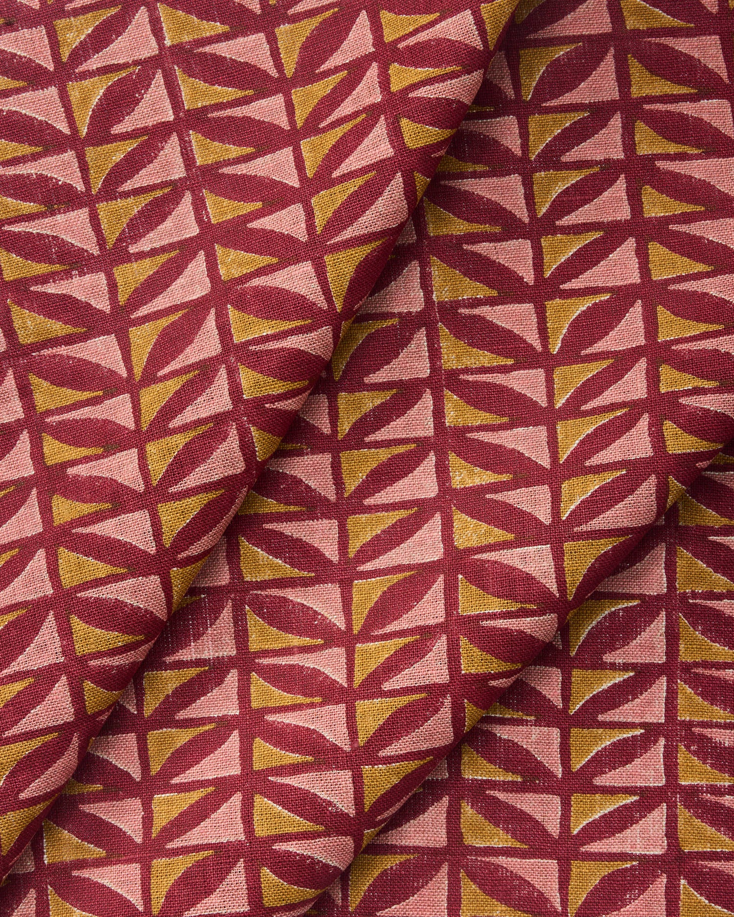 Draped close-up of fabric with geometric pattern in pink and ochre on a crimson field. 