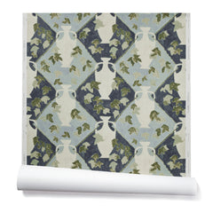 Partially unrolled wallpaper in a large, painterly vase and leaf print over a repeating diamond background in shades of blue.
