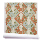 Partially unrolled wallpaper in a large, painterly vase and leaf print over a repeating diamond background in shades of green and blue and rust.