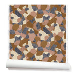 Partially unrolled wallpaper in a painterly geometric pattern in shades of mauve, brown, cream and navy.