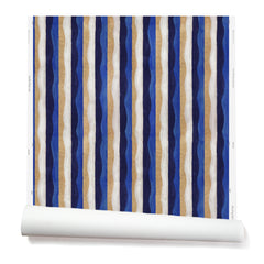 Partially unrolled wallpaper in a curvy hand-painted stripe pattern in blue, gold, white and navy.