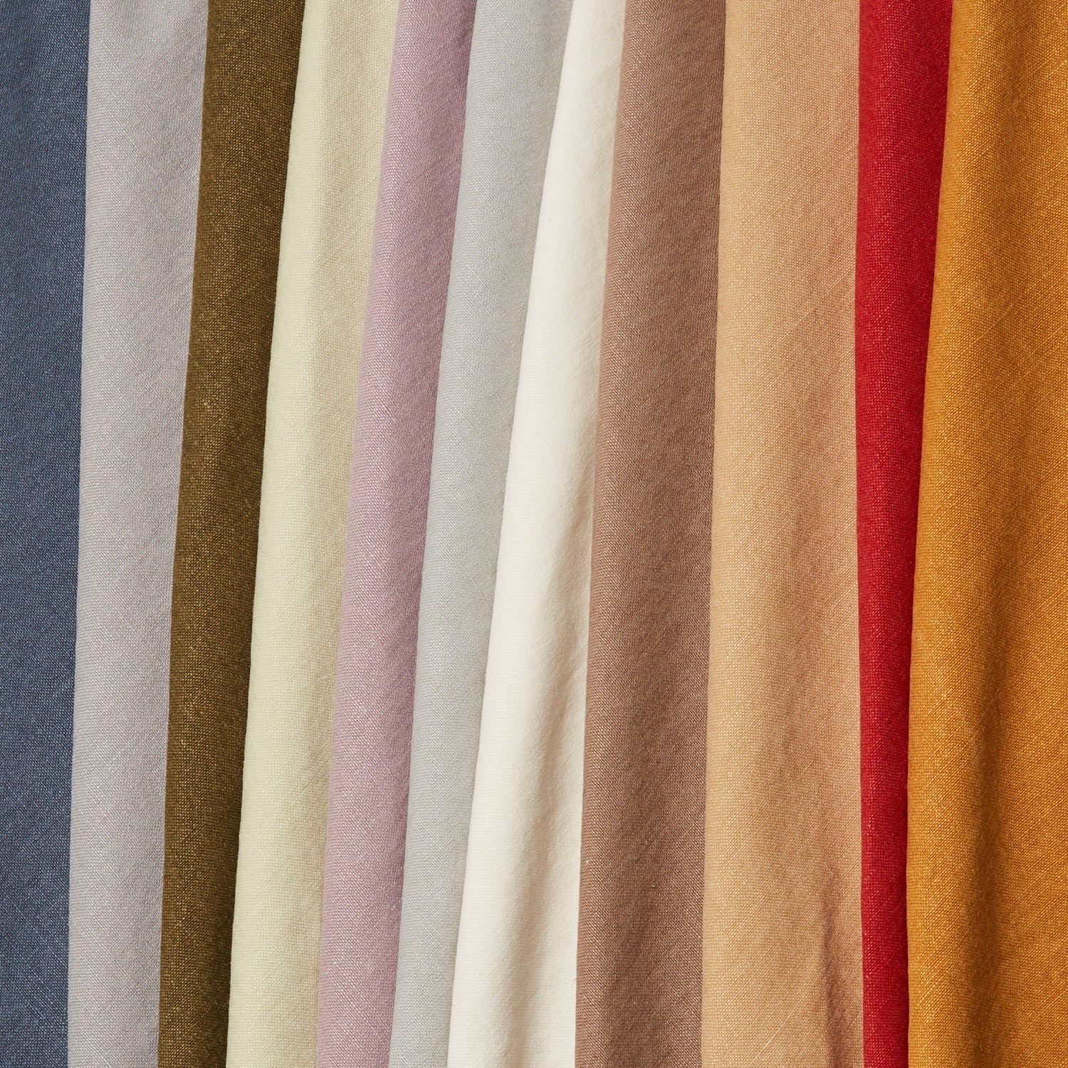 A row of folded linen fabrics in an assortment of solid colors including blue, tans, brown, cream, red and orange.