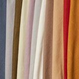 A row of folded linen fabrics in an assortment of solid colors including blue, tans, brown, cream, red and orange.