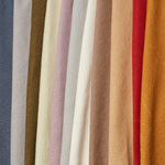 A row of folded linen fabrics in an assortment of solid colors including blue, tans, brown, cream, red and orange.