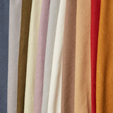 A row of folded linen fabrics in an assortment of solid colors including blue, tans, brown, cream, red and orange.