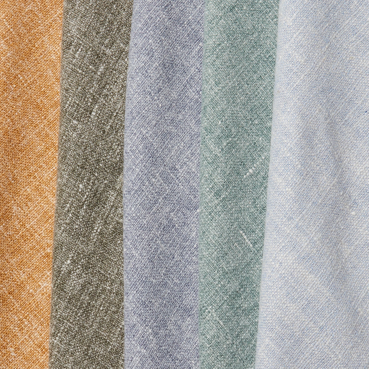 A row of folded linen swatches in mottled shades of blue, green, gray, brown and mustard.