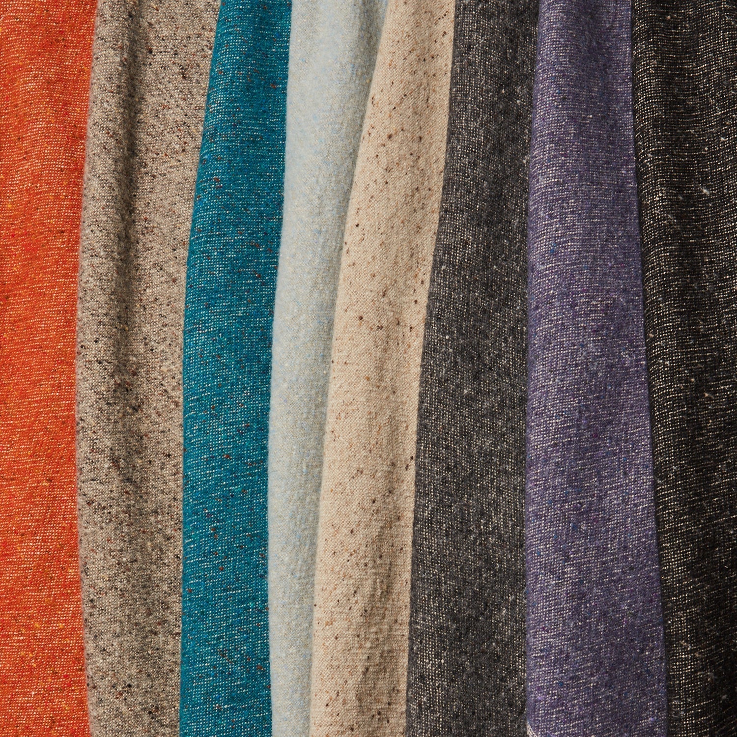 A row of folded linen-wool swatches in a variety of flecked colorways including tans, grays, reds and purples.