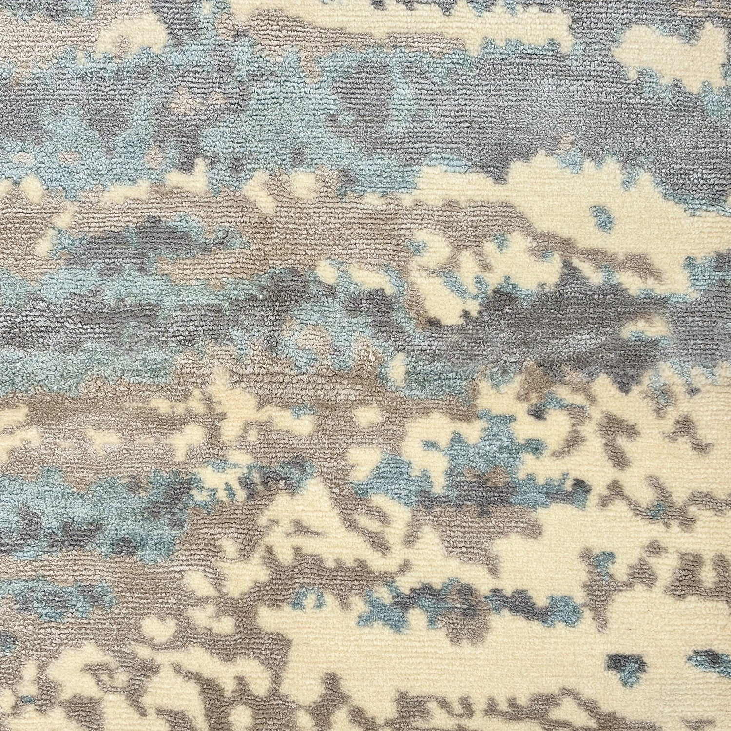 Detail of a woolblend rug in grey, cream and acqua in an abstract textural pattern.