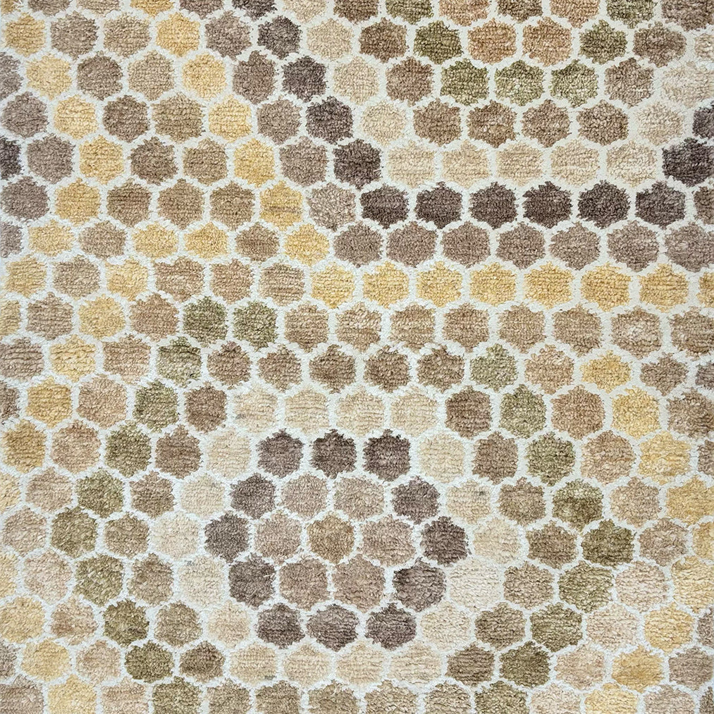 Detail of a handknotted rug with a classic hexagon pattern in shades of tan, yellow, white and oatmeal. 