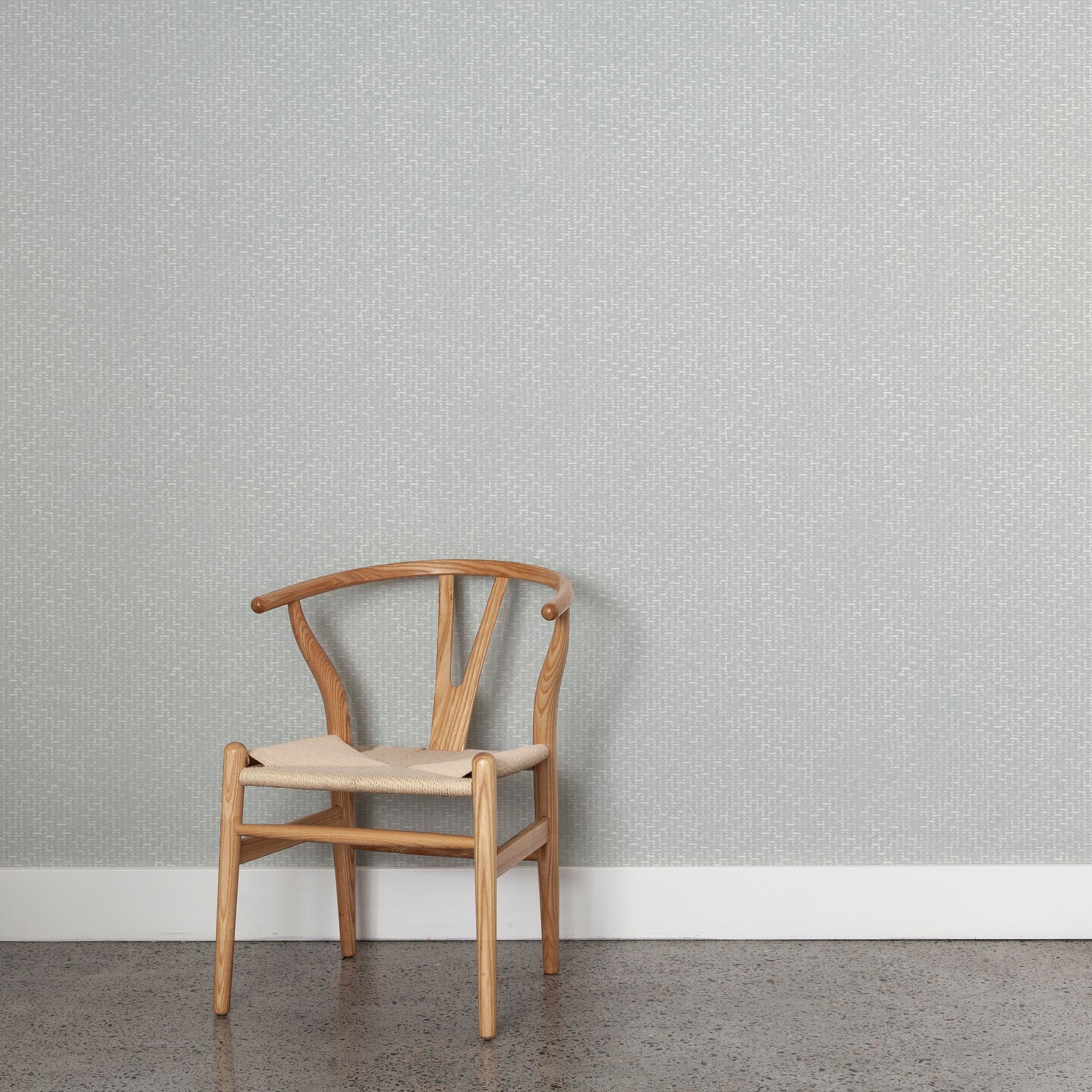 A wooden chair stands in front of a wall papered in a small-scale grid pattern in shades of pale blue.