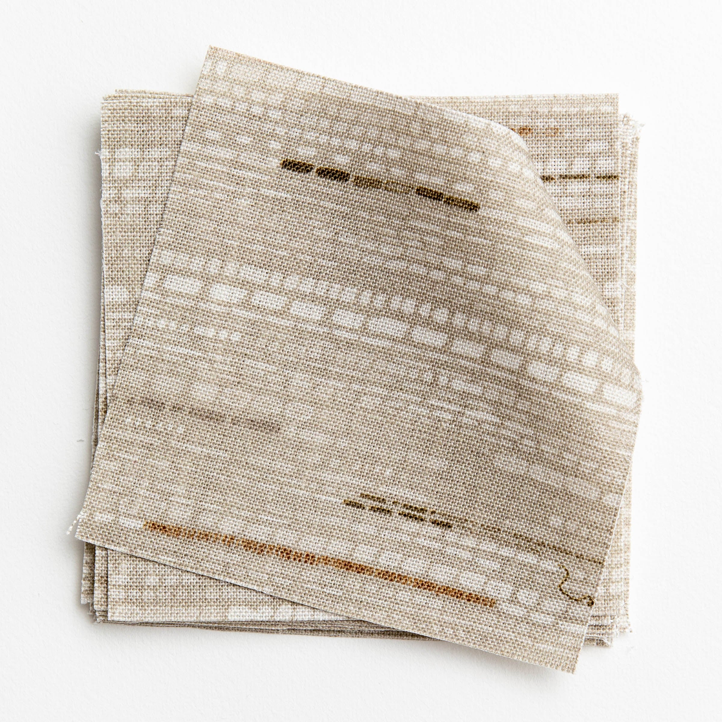 A stack of fabric swatches in a textural striped pattern in shades of white, cream and gray.