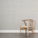 A wooden chair stands in front of a wall papered in a textural striped pattern in shades of gray, white and tan.