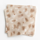 A stack of fabric swatches in a painterly animal print in cream and brown on a tan field.