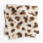 A stack of fabric swatches in a painterly animal print in brown and tan on a cream field.