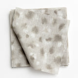 A stack of fabric swatches in a painterly animal print in white and gray on a light gray field.