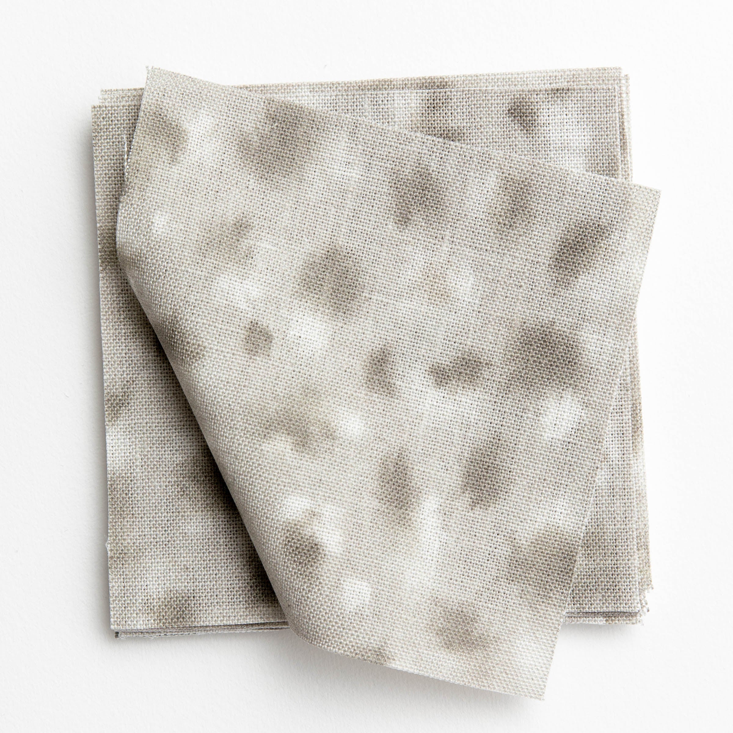 A stack of fabric swatches in a painterly animal print in white and gray on a light gray field.