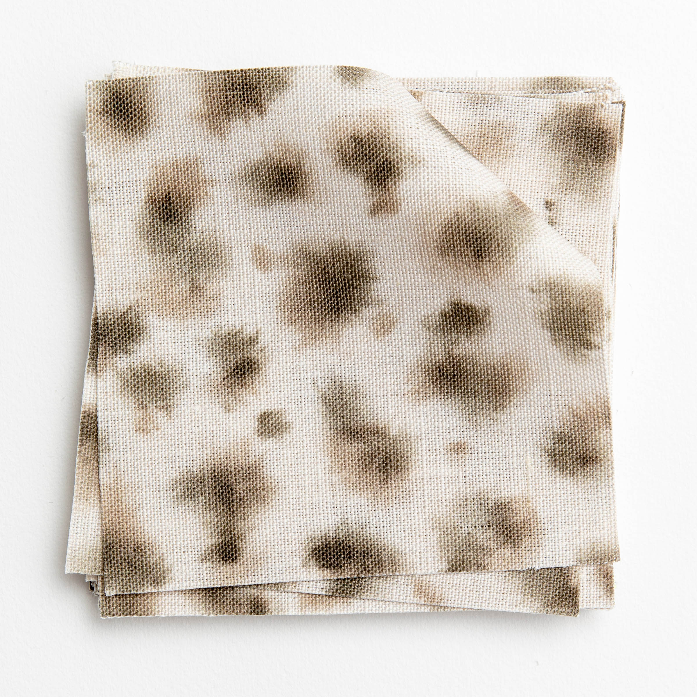 A stack of fabric swatches in a painterly animal print in brown and gray on a cream field.