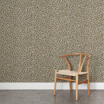 A wooden chair stands in front of a wall papered in a painterly animal print in white and brown on a gray field.