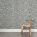A wooden chair stands in front of a wall papered in a painterly animal print in white and tan on a blue-gray field.
