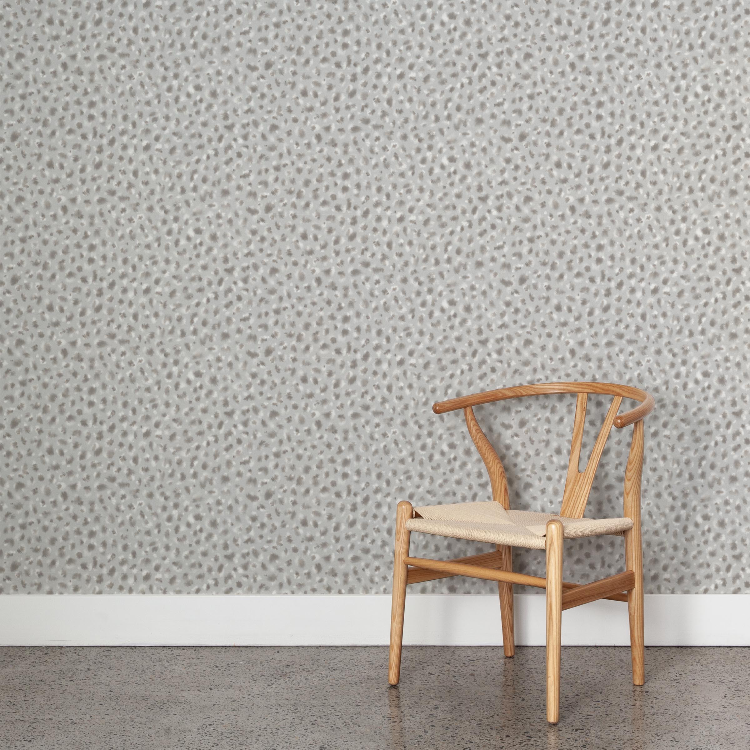 A wooden chair stands in front of a wall papered in a painterly animal print in white and gray on a light gray field.