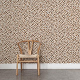 A wooden chair stands in front of a wall papered in a painterly animal print in shades of brown on a cream field.