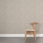 A wooden chair stands in front of a wall papered in a painterly animal print in white and brown on a sable field.