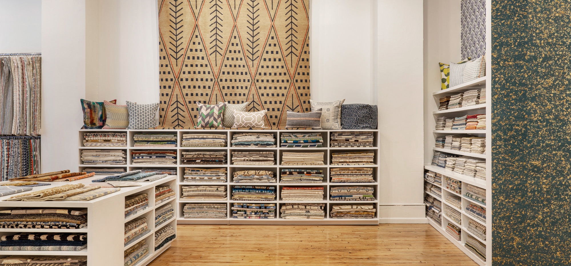 Photo of an interior design showroom with wooden shelves full of fabric and wallpaper swatches, and topped with throw pillows.