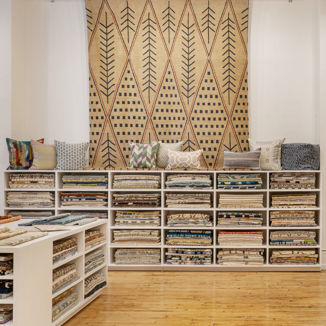 Photo of an interior design showroom with wooden shelves full of fabric and wallpaper swatches, and topped with throw pillows.