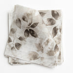 A stack of fabric swatches in a painterly leaf print in shades of brown and gray with a mottled white overlay.