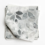 A stack of fabric swatches in a painterly leaf print in shades of gray with a mottled white overlay.