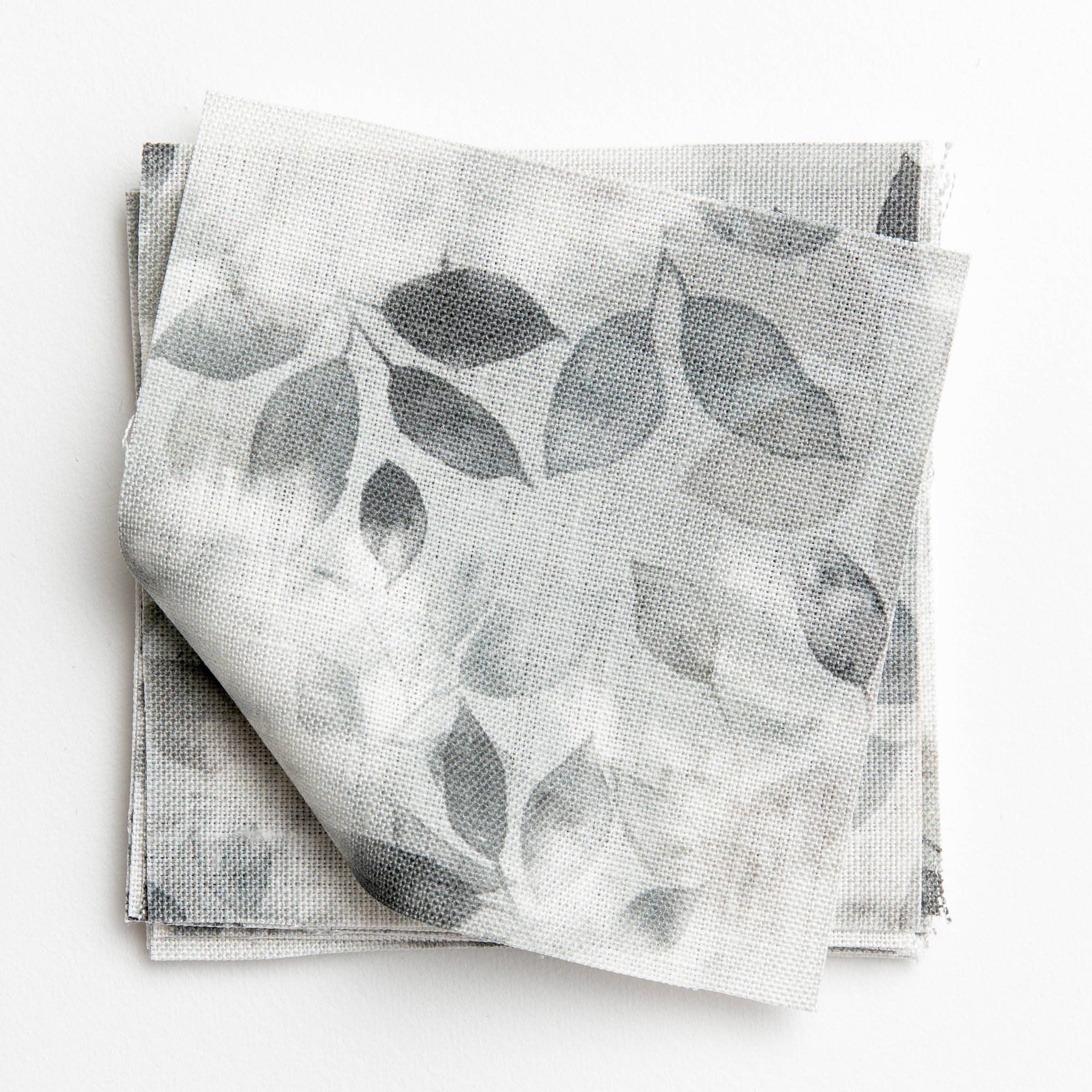 A stack of fabric swatches in a painterly leaf print in shades of gray with a mottled white overlay.