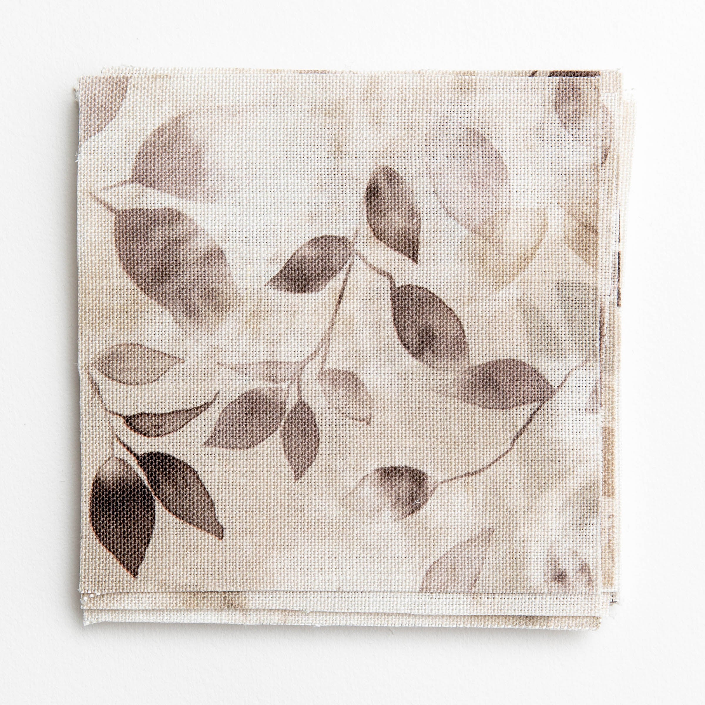 A stack of fabric swatches in a painterly leaf print in shades of tan and purple with a mottled white overlay.