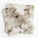 A stack of fabric swatches in a painterly leaf print in shades of tan and brown with a mottled white overlay.