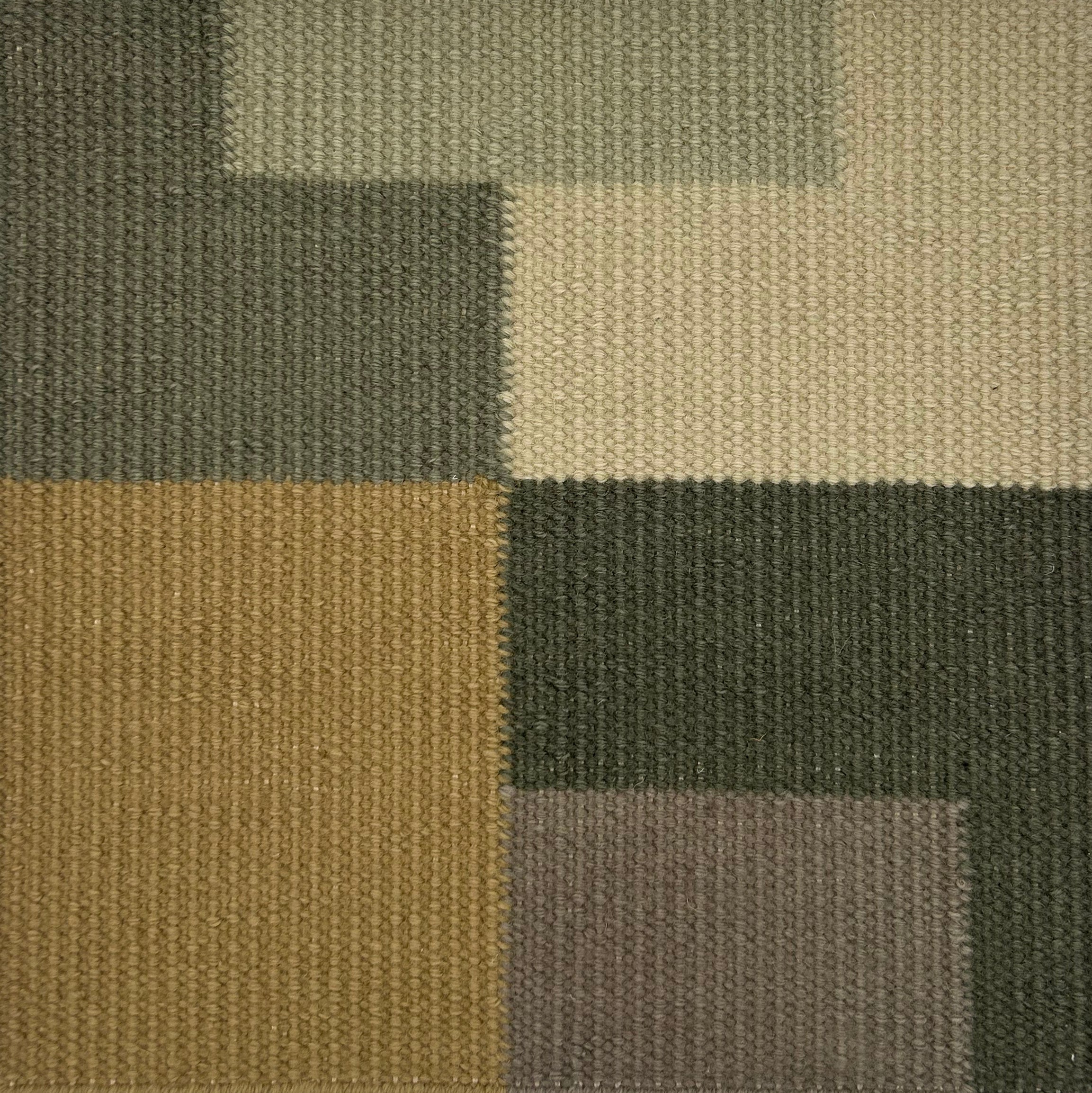 Close-up of a carpet swatch with a patchwork pattern in green, brown, and gray.